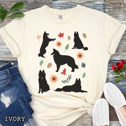 Beige cottagecore style dog lover t-shirt with Belgian Sheepdog silhouettes and colorful leaves on a wooden surface.