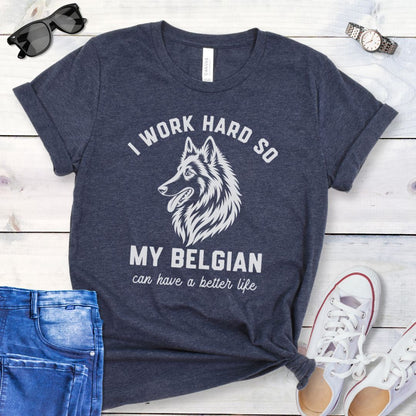 Heather navy blue unisex t-shirt for Belgian Sheepdog lovers with breed head study graphic and humorous text 'I work hard so my Belgian can have a better life', shown on a wooden surface with jeans and shoes. 
