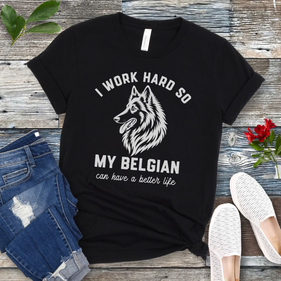 Black unisex t-shirt for Belgian Sheepdog lovers with breed head study graphic and humorous text 'I work hard so my Belgian can have a better life', shown on a wooden surface with jeans and shoes. 