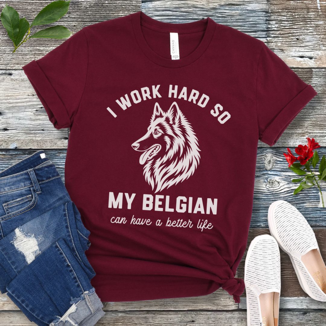 Maroon unisex t-shirt for Belgian Sheepdog lovers with breed head study graphic and humorous text 'I work hard so my Belgian can have a better life', shown on a wooden surface with jeans and shoes. 