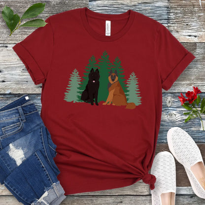 Cardinal red Belgian Shepherd t-shirt with Belgian Sheepdog and Tervuren sitting in front of evergreen trees, shown on a wooden surface with jeans and shoes.
