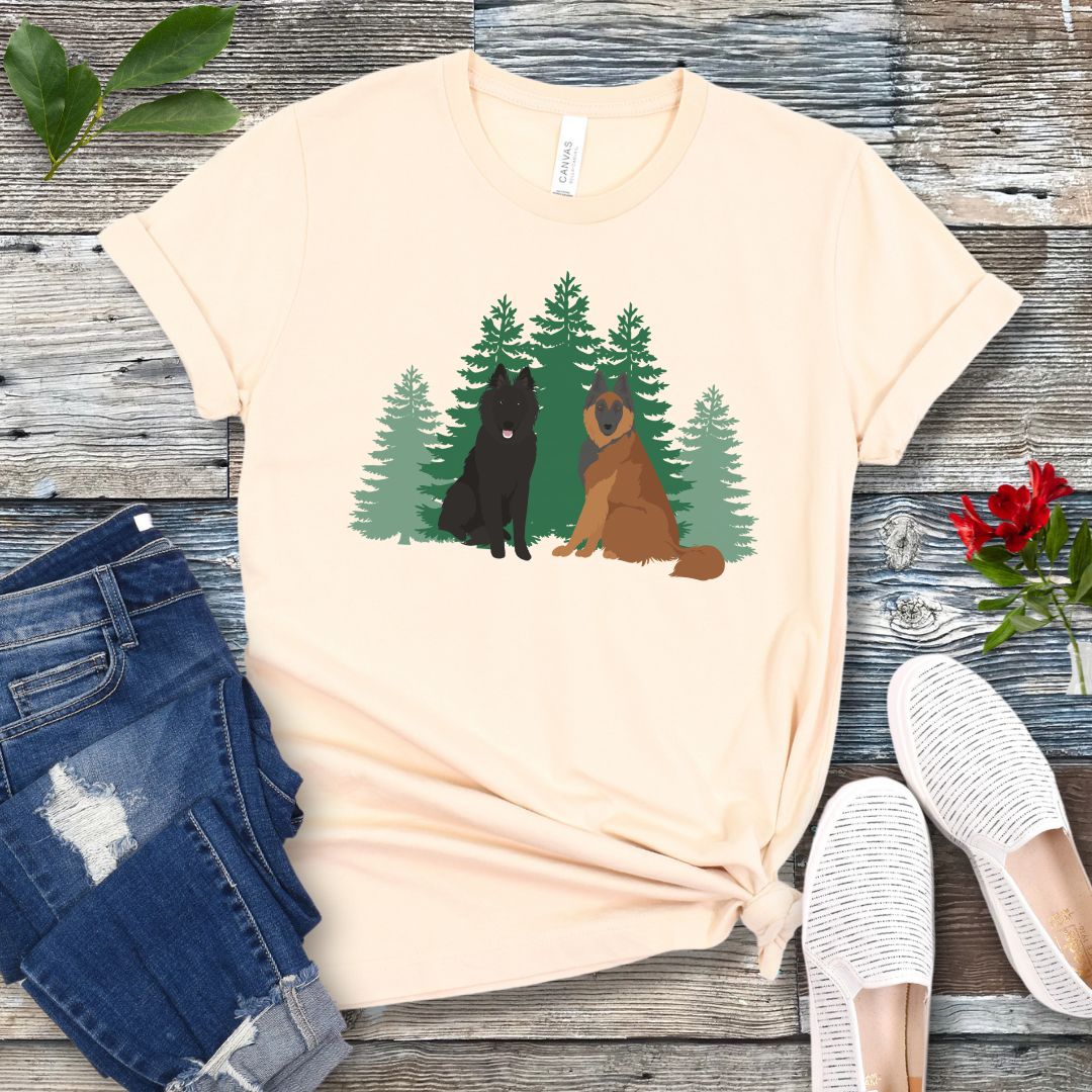 Beige Belgian Shepherd t-shirt with Belgian Sheepdog and Tervuren sitting in front of evergreen trees, shown on a wooden surface with jeans and shoes.