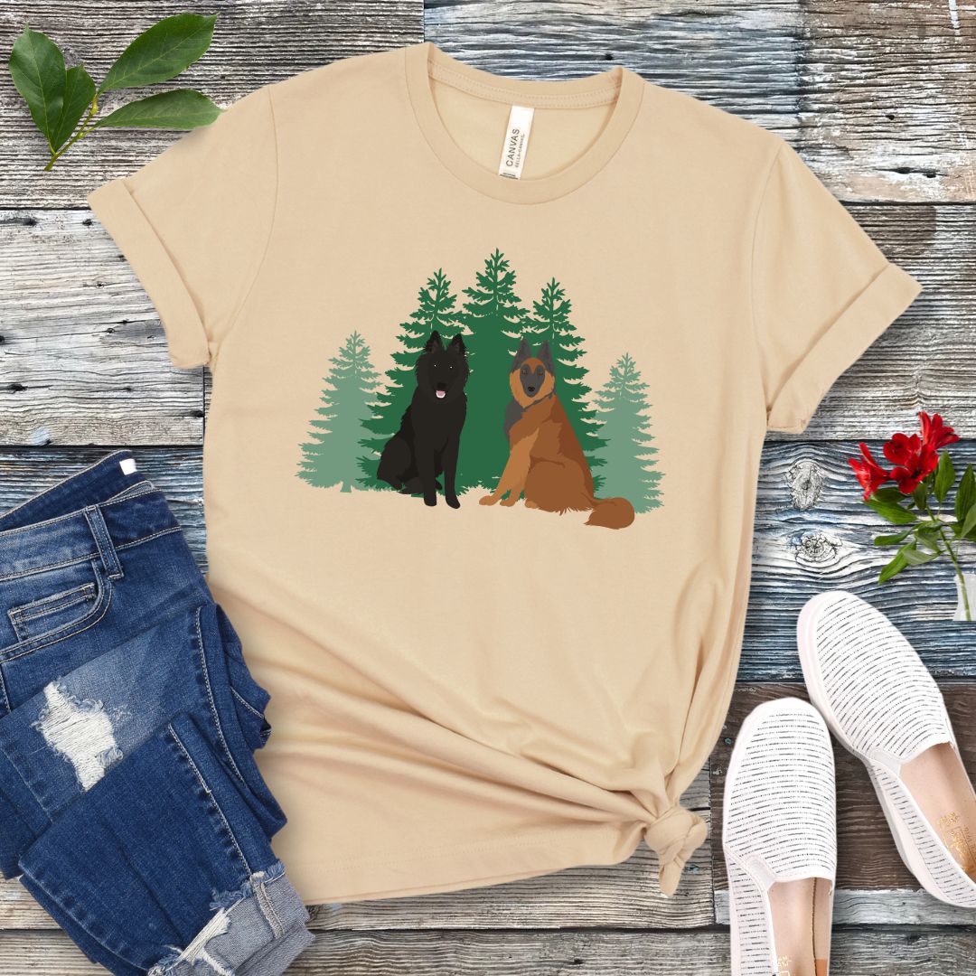 Cream-colored Belgian Shepherd t-shirt with Belgian Sheepdog and Tervuren sitting in front of evergreen trees, shown on a wooden surface with jeans and shoes.