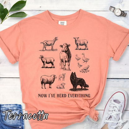 Orange Comfort Colors t-shirt for Belgian Sheepdog lovers with vintage  illustrations of farm animals and a Groenendael dog, with the humorous text 'Now I've Herd Everything', shown on a wooden surface with denim jeans and flowers.