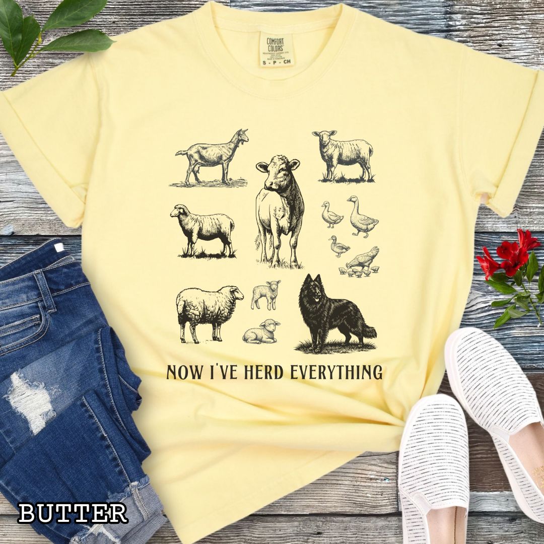 Yellow Comfort Colors t-shirt for Belgian Sheepdog lovers with vintage  illustrations of farm animals and a Groenendael dog, with the humorous text 'Now I've Herd Everything', shown on a wooden surface with denim jeans and flowers.