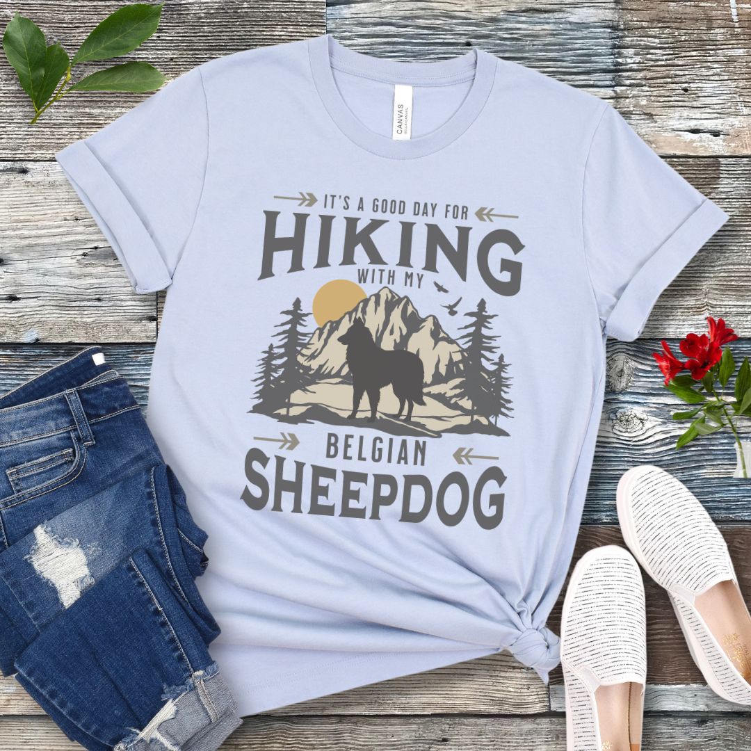 Light blue Belgian Sheepdog t-shirt with vintage-style mountain wilderness graphic, Belgian Sheepdog silhouette and "Hiking With My Belgian Sheepdog' text on a wooden surface with jeans and shoes.