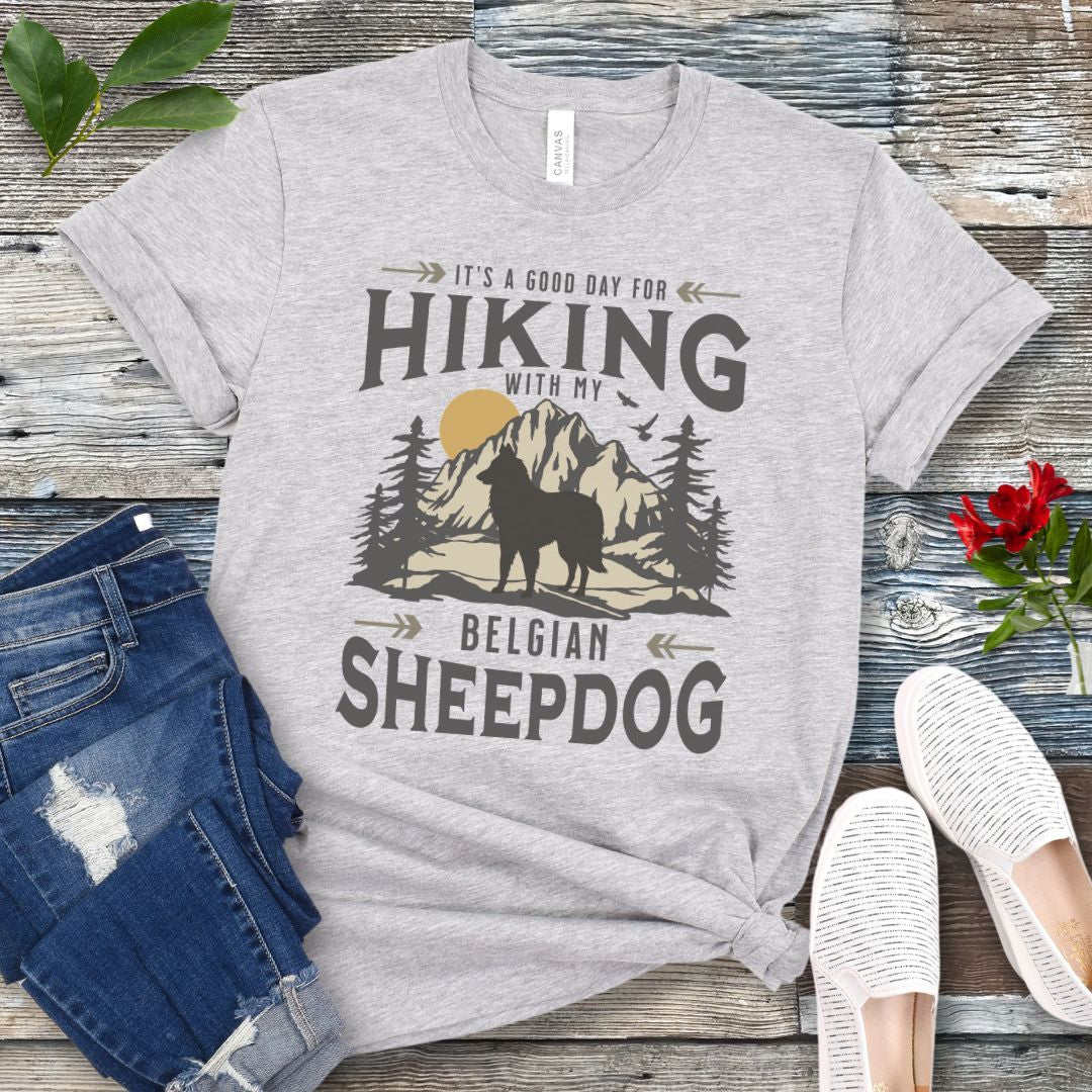 Athletic grey Belgian Sheepdog t-shirt with vintage-style mountain wilderness graphic, Belgian Sheepdog silhouette and "Hiking With My Belgian Sheepdog' text on a wooden surface with jeans and shoes.