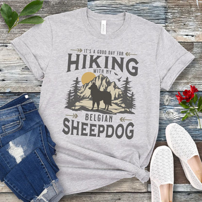 Athletic grey Belgian Sheepdog t-shirt with vintage-style mountain wilderness graphic, Belgian Sheepdog silhouette and "Hiking With My Belgian Sheepdog' text on a wooden surface with jeans and shoes.