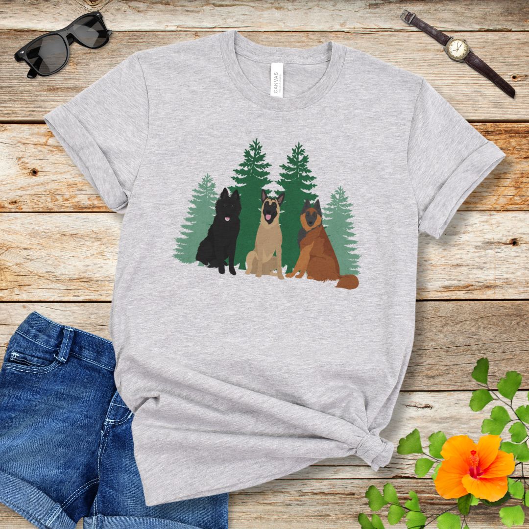 A grey Bella Canvas 3001 unisex short sleeve t-shirt with an image of three Belgian Shepherds (Belgian Sheepdog, Malinois and Tervuren) and evergreen trees on the front, displayed on a wooden surface with a pair of jeans and white shoes in the background.