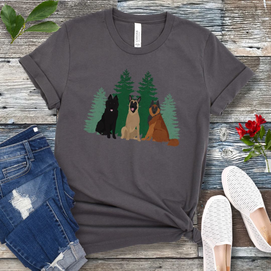 A dark grey Bella Canvas 3001 unisex short sleeve t-shirt with an image of three Belgian Shepherds (Belgian Sheepdog, Malinois and Tervuren) and evergreen trees on the front, displayed on a wooden surface with a pair of jeans and white shoes in the background.