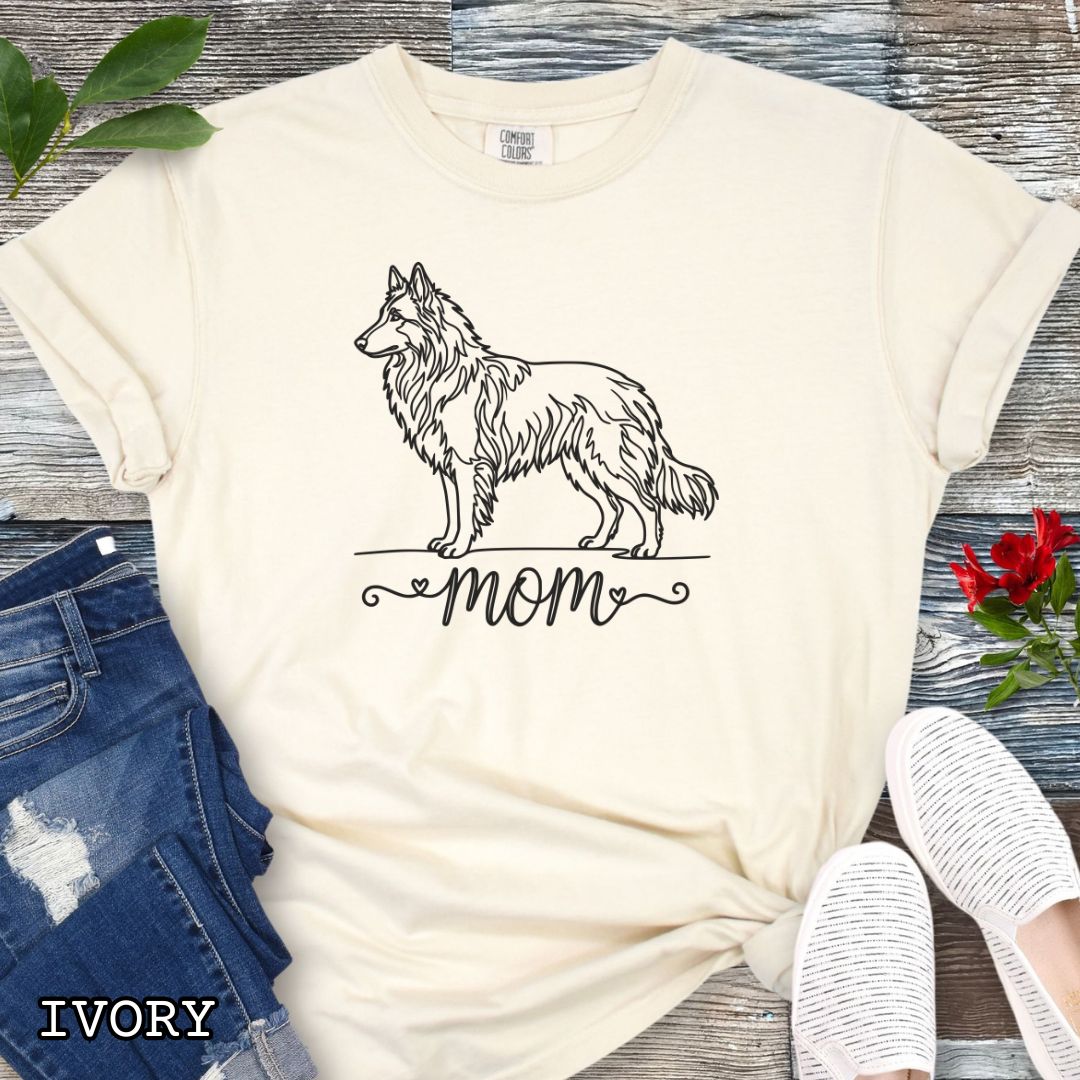 Beige Comfort Colors t-shirt for Belgian Tervuren and Groenendael lovers, with a line art Belgian Shepherd graphic and 'mom' text in script lettering, shown on a wooden surface.