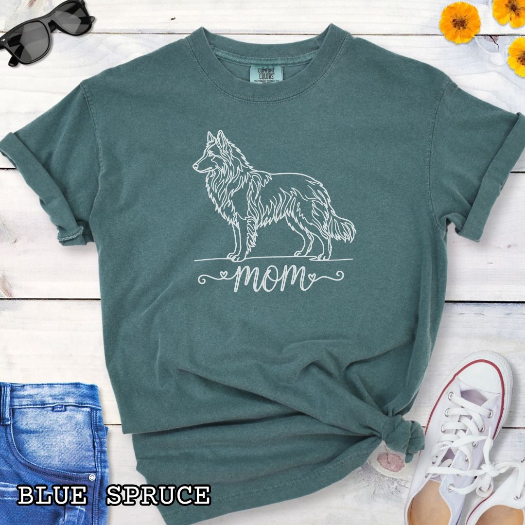 Green Comfort Colors t-shirt for Belgian Tervuren and Groenendael lovers, with a line art Belgian Shepherd graphic and 'mom' text in script lettering, shown on a wooden surface.