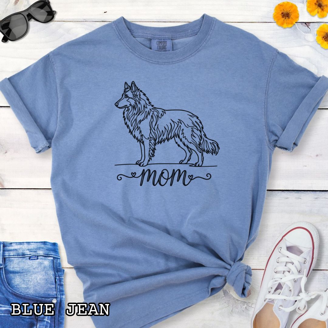 Blue Comfort Colors t-shirt for Belgian Tervuren and Groenendael lovers, with a line art Belgian Shepherd graphic and 'mom' text in script lettering, shown on a wooden surface.