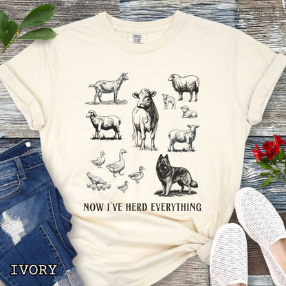 Beige Comfort Colors t-shirt for Belgian Tervuren lovers with vintage farm animal illustrations and a Belgian Tervuren dog, with the humorous text 'Now I've Herd Everything', shown on a wooden surface with denim jeans and flowers.