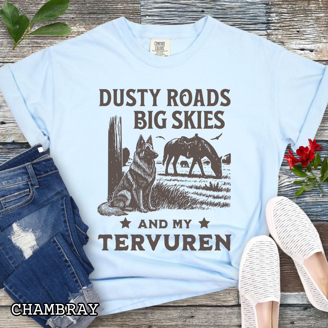 Light blue Comfort Colors t-shirt featuring a Western-style design with grazing horse, rustic fence, and a Belgian Tervuren illustration; text reads “Dusty Roads, Big Skies, and My Tervuren.”