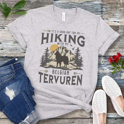 Grey Belgian Tervuren t-shirt with vintage-style mountain wilderness graphic, Tervuren dog silhouette and "Hiking With My Belgian Tervuren' text on a wooden surface with jeans and shoes.