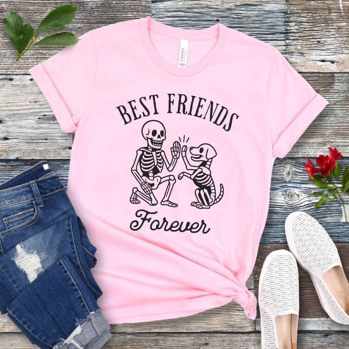 A pink dog lover t-shirt with 'BEST FRIENDS FOREVER' text and a graphic of a skeleton person high-fiving a skeleton dog. The t-shirt is presented with denim jeans and white shoes in the background.