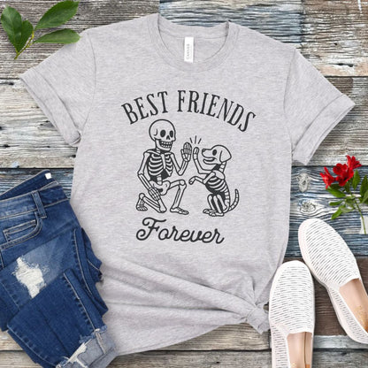 A light grey dog lover t-shirt with 'BEST FRIENDS FOREVER' text and a graphic of a skeleton person high-fiving a skeleton dog. The t-shirt is presented with denim jeans and white shoes in the background.