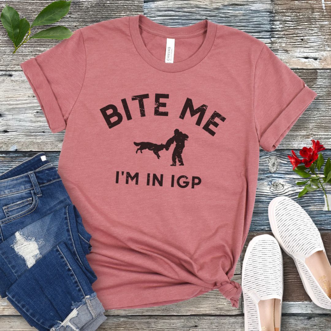 Mauve IGP dog sport t-shirt with 'Bite Me I'm in IGP' text and bite work graphic on a wooden surface with jeans and shoes.