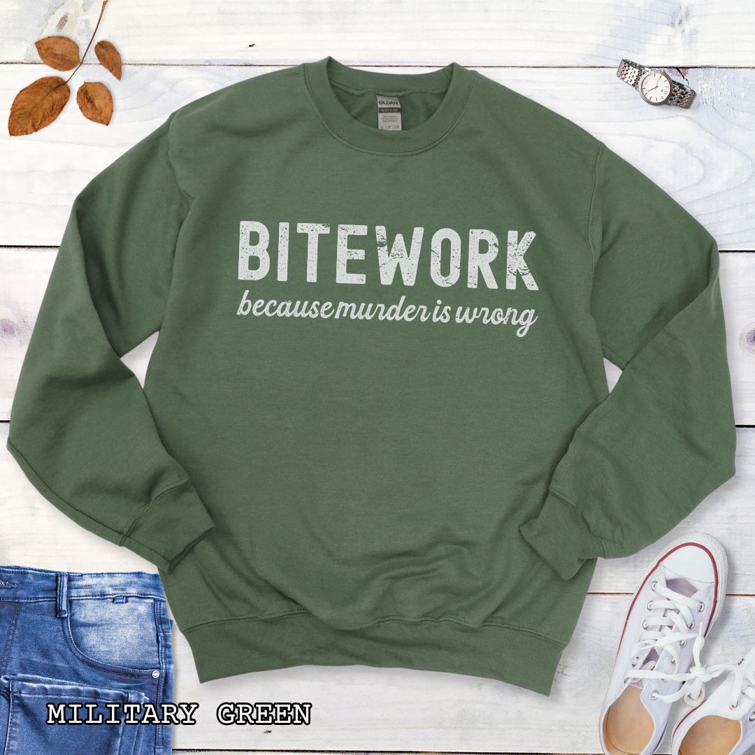 Military green Schutzhund sweatshirt with 'BITEWORK because murder is wrong' text on a wooden surface with jeans and shoes.