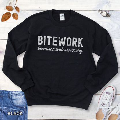 Black Schutzhund sweatshirt with 'BITEWORK because murder is wrong' text on a wooden surface with jeans and shoes.