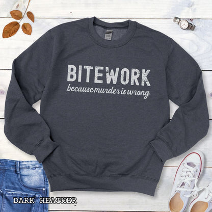 Dark grey Schutzhund sweatshirt with 'BITEWORK because murder is wrong' text on a wooden surface with jeans and shoes.