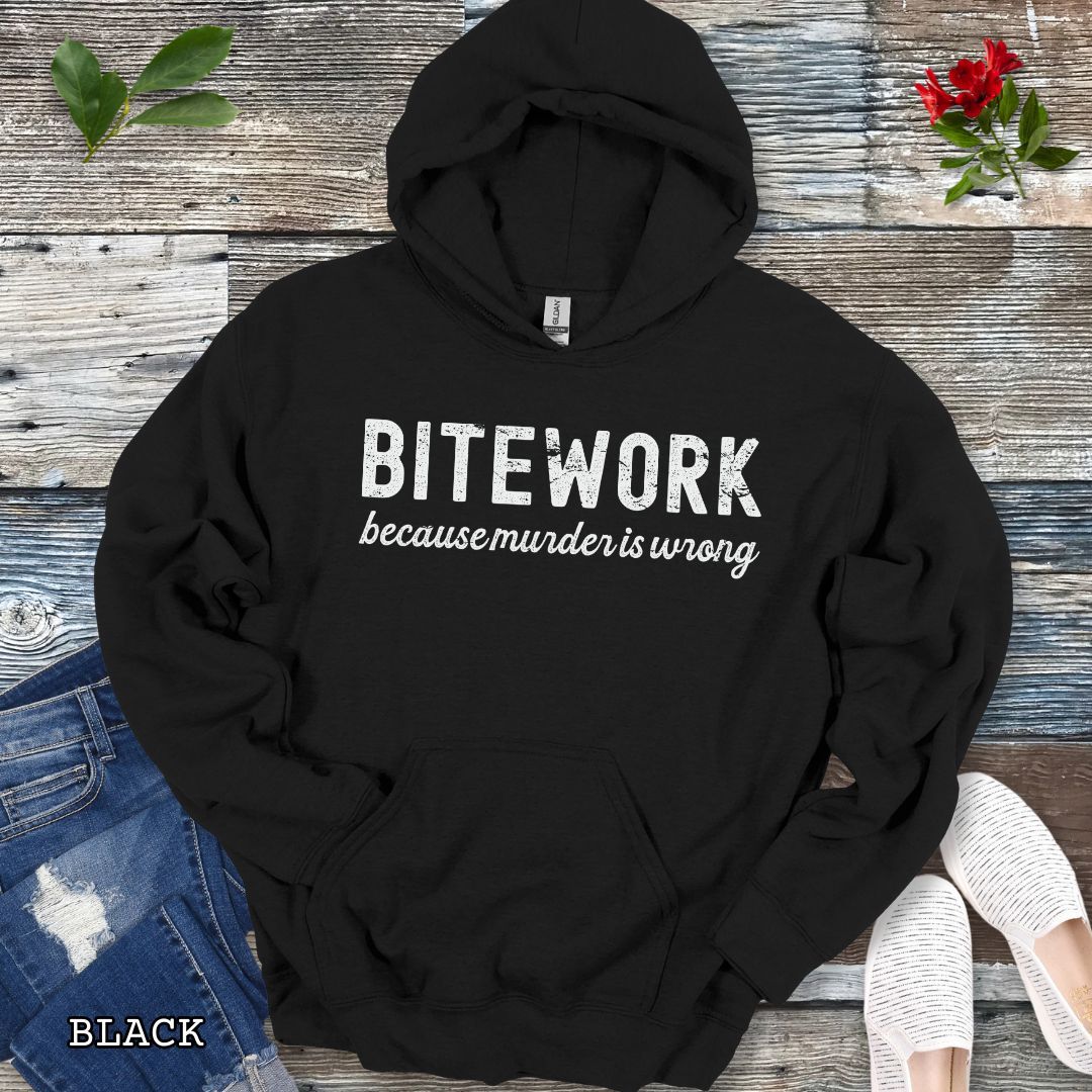 Black K9 bite sport hoodie with 'BITEWORK because murder is wrong' text on a wooden surface with jeans and shoes.