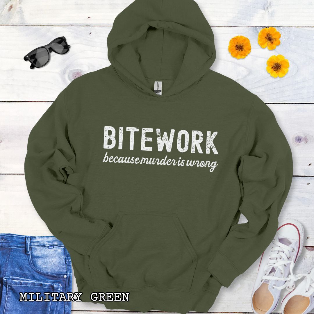 Military green Schutzhund hoodie with 'BITEWORK because murder is wrong' text on a wooden surface with jeans and shoes.