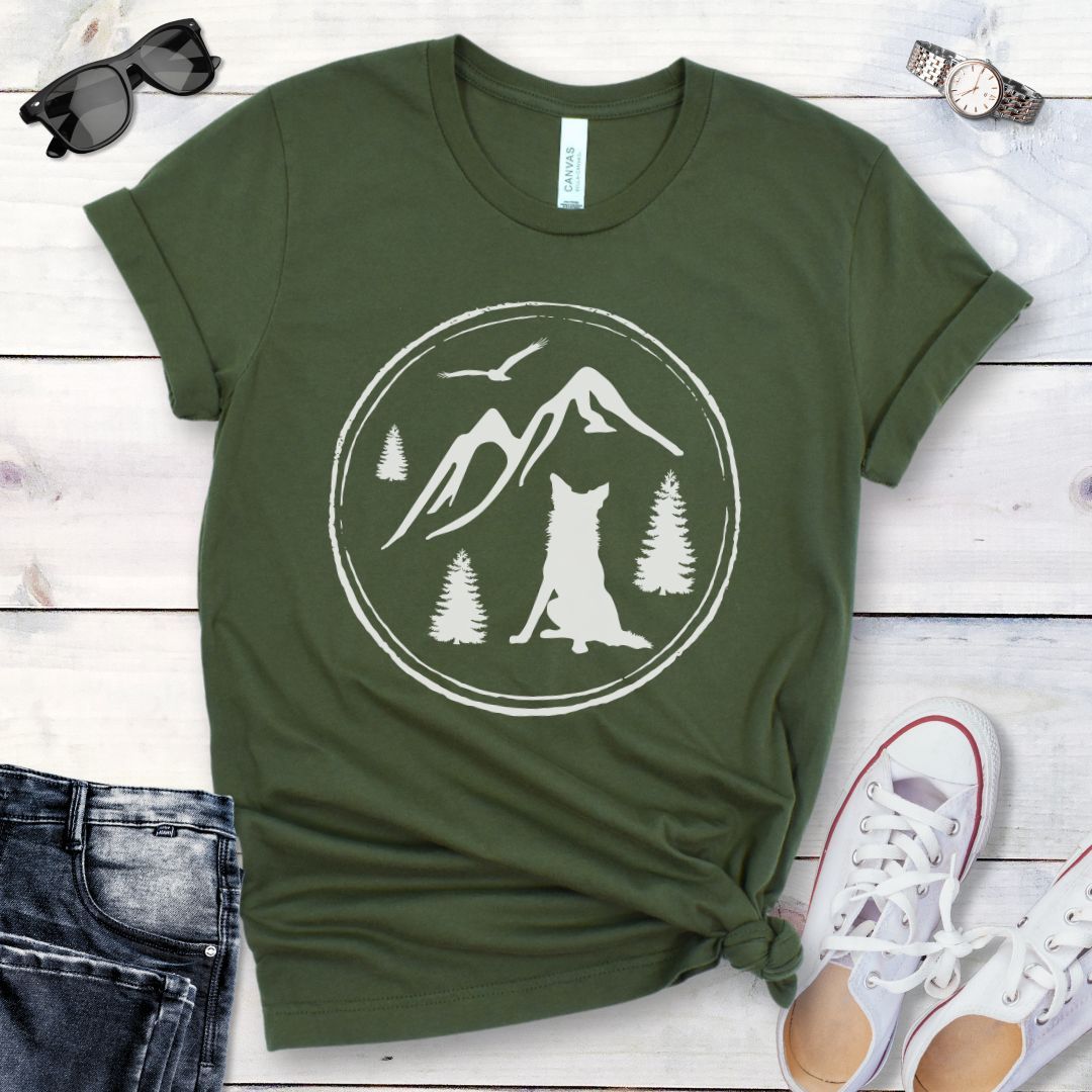 Military green t-shirt for outdoorsy dog lovers, with a minimalist mountain scene and Border Collie, shown on a wooden surface with jeans and sneakers.