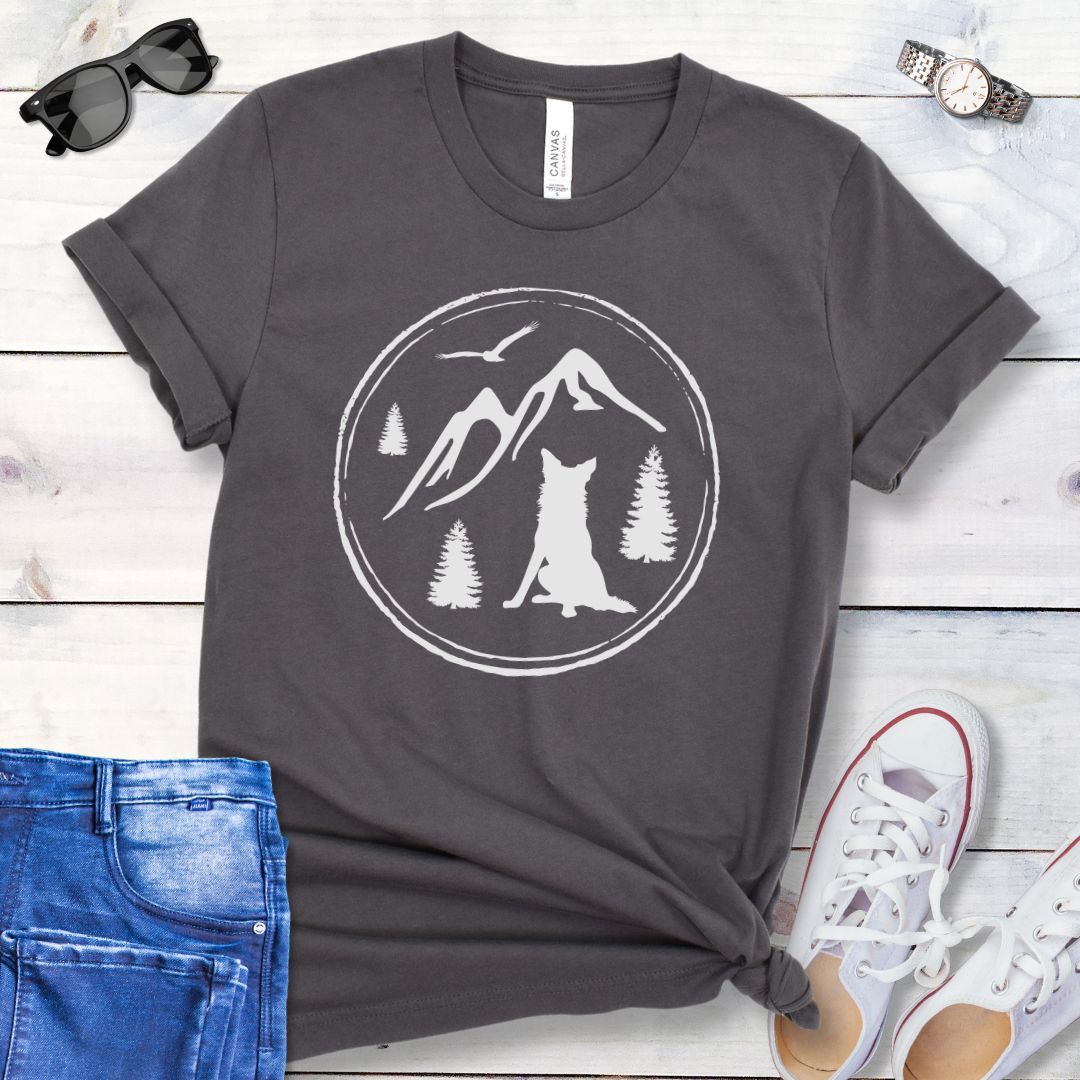 Grey t-shirt for outdoorsy dog lovers, with a minimalist mountain scene and Border Collie, shown on a wooden surface with jeans and sneakers.