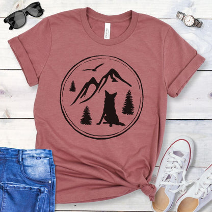 Mauve t-shirt for outdoorsy dog lovers, with a minimalist mountain scene and Border Collie, shown on a wooden surface with jeans and sneakers.