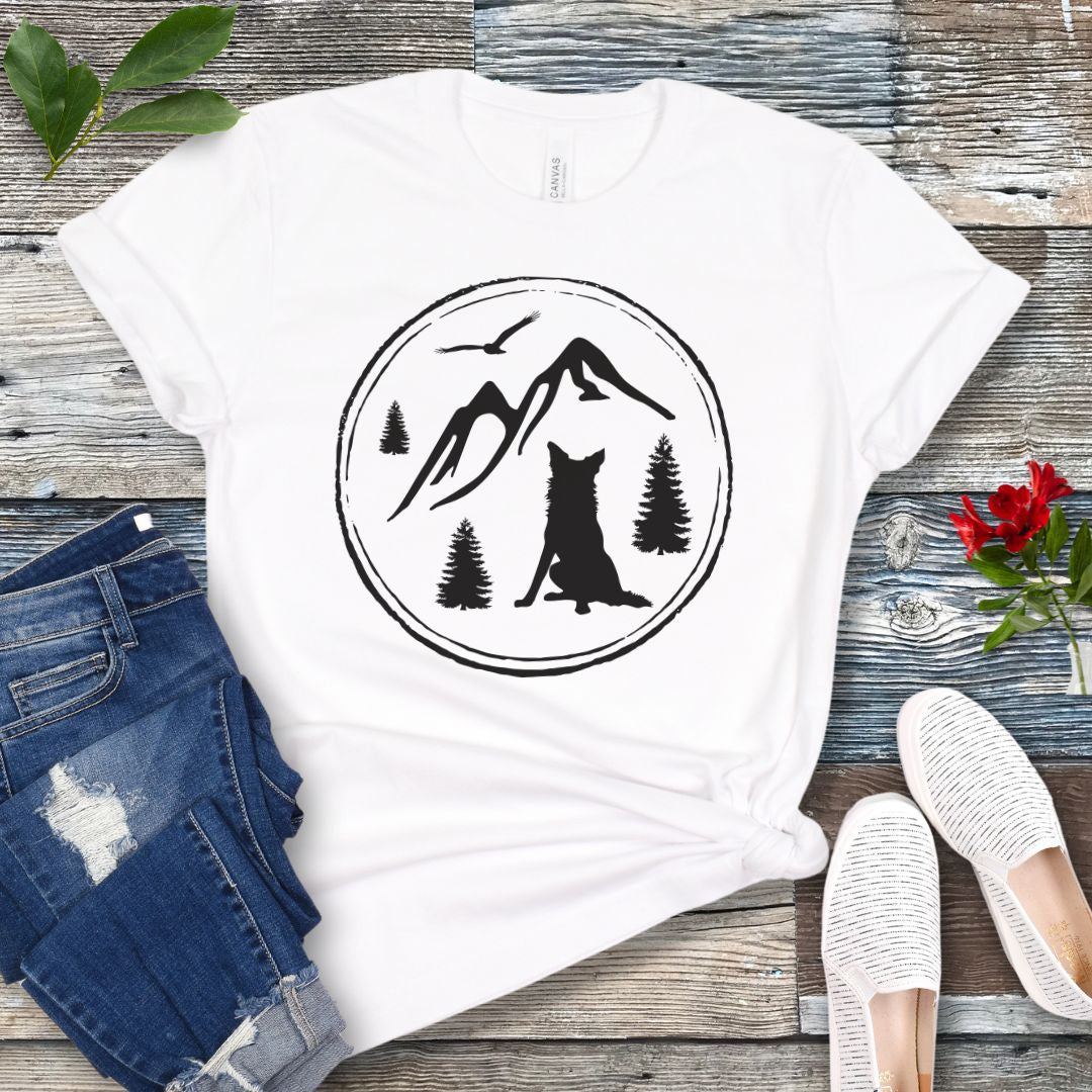 White t-shirt for outdoorsy dog lovers, with a minimalist mountain scene and Border Collie, shown on a wooden surface with jeans and sneakers.