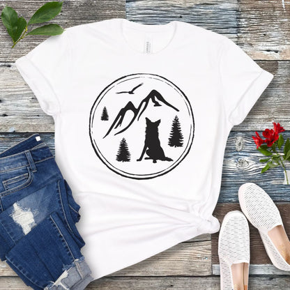 White t-shirt for outdoorsy dog lovers, with a minimalist mountain scene and Border Collie, shown on a wooden surface with jeans and sneakers.