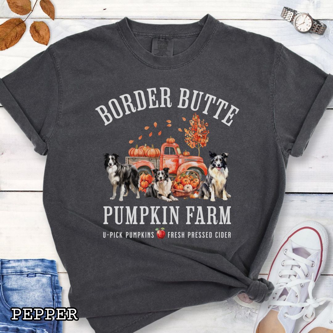 Dark grey fall-theme t-shirt for Border Collie lovers with 'Border Butte Pumpkin Farm' design featuring Border Collies, fall foliage and a pumpkin truck, shown on a wooden surface.