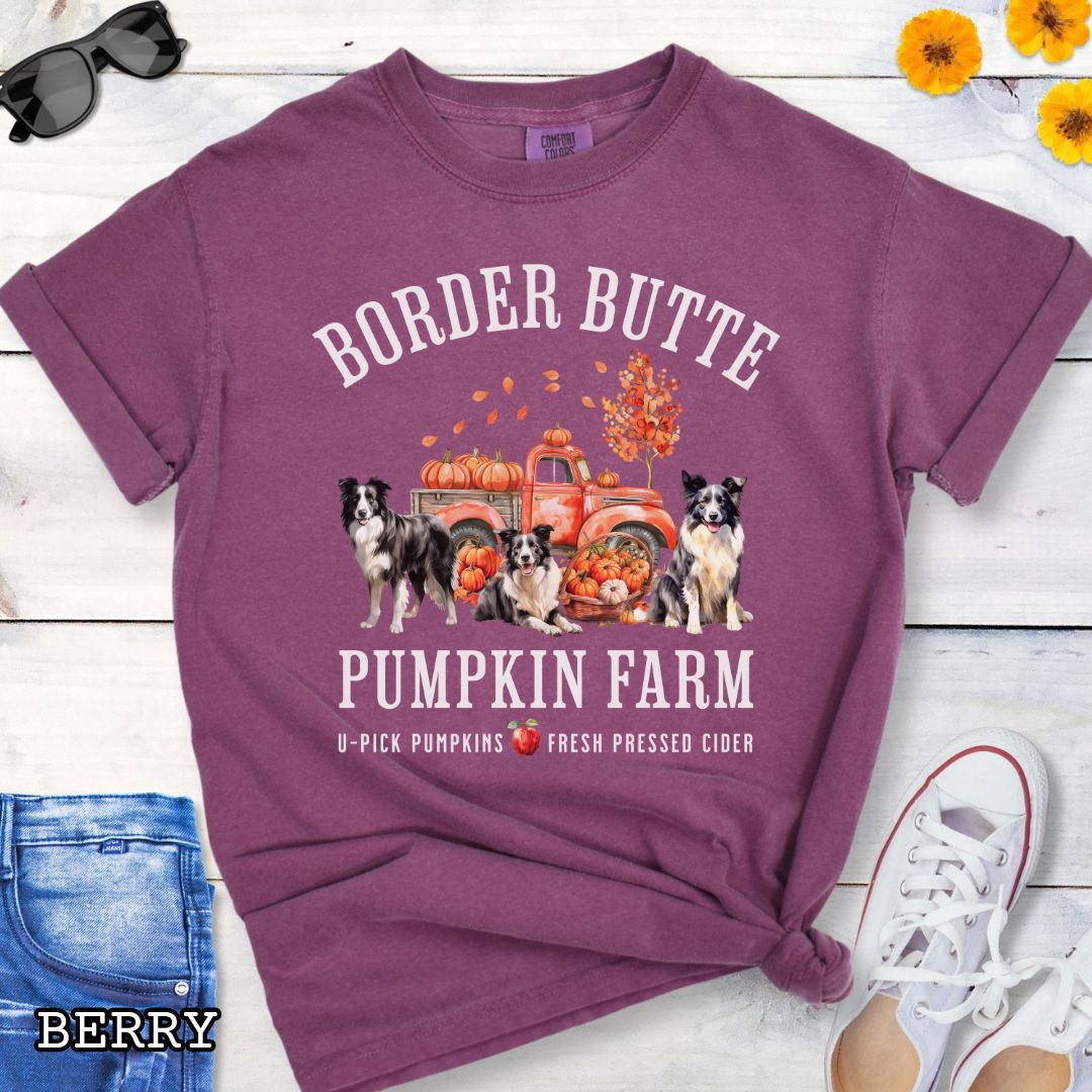 Berry-colored fall-theme t-shirt for Border Collie lovers with 'Border Butte Pumpkin Farm' design featuring Border Collies, fall foliage and a pumpkin truck, shown on a wooden surface.