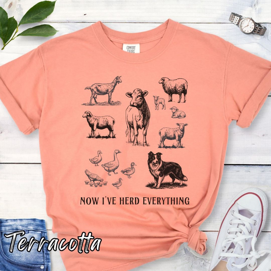 Orange Comfort Colors t-shirt for Border Collie lovers with vintage farm animal illustrations and a Border Collie dog, with the humorous text 'Now I've Herd Everything', shown on a wooden surface with denim jeans and flowers.