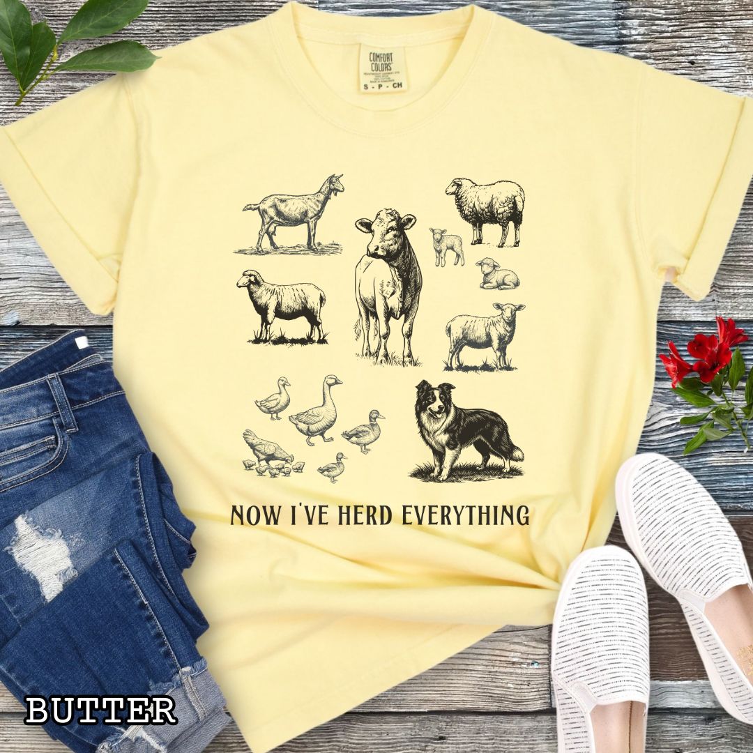 Yellow Comfort Colors t-shirt for Border Collie lovers with vintage farm animal illustrations and a Border Collie dog, with the humorous text 'Now I've Herd Everything', shown on a wooden surface with denim jeans and flowers.