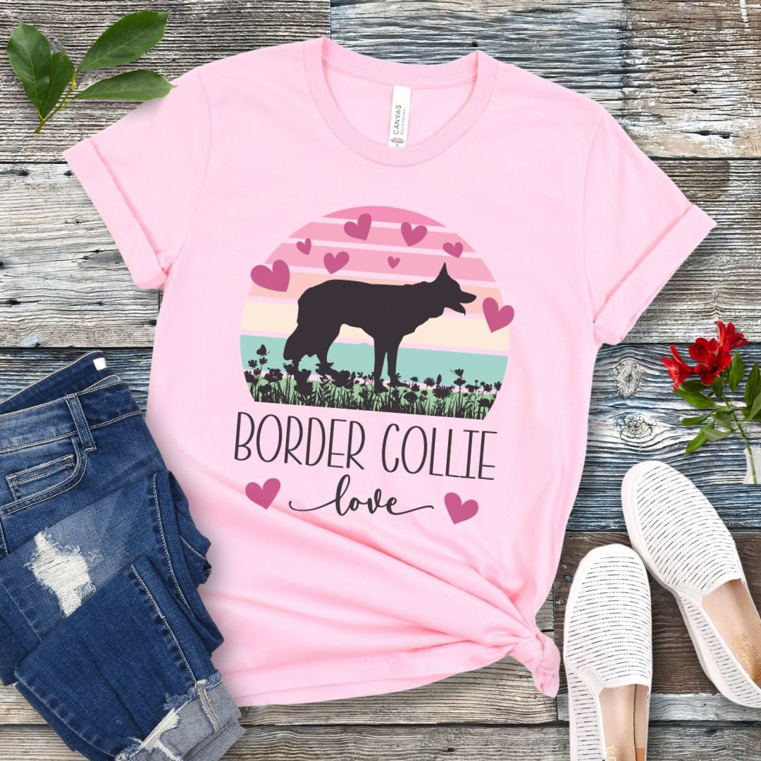 Pink t-shirt with Border Collie silhouette amid pastel vintage sunset and hearts, with the text 'Border Collie love'. Shown on a wooden surface with denim shorts and white shoes.