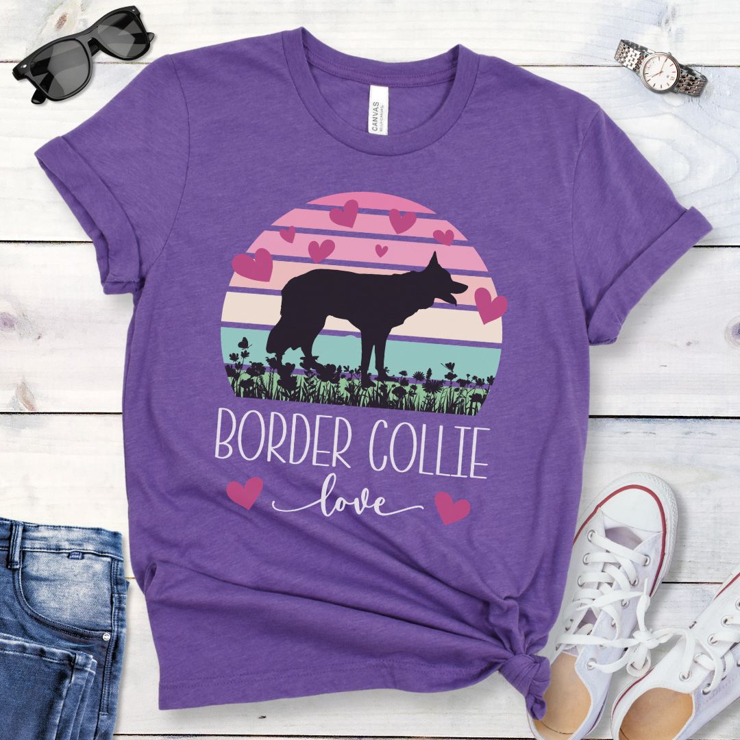 Purple t-shirt with Border Collie silhouette amid pastel vintage sunset and hearts, with the text 'Border Collie love'. Shown on a wooden surface with denim shorts and white shoes.