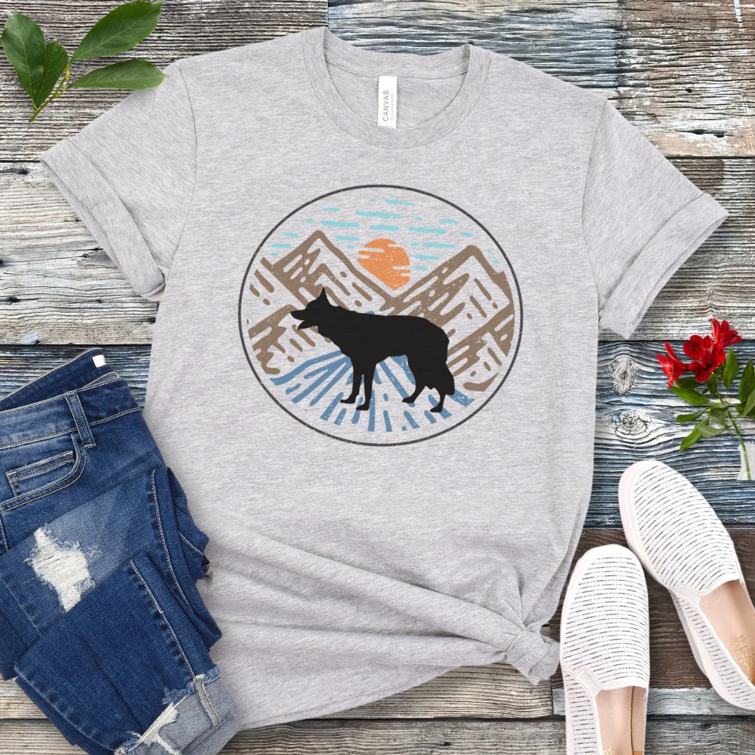 Grey t-shirt with a Border Collie in a vintage style mountain scene at sunset, shown on a wooden surface with jeans and shoes.