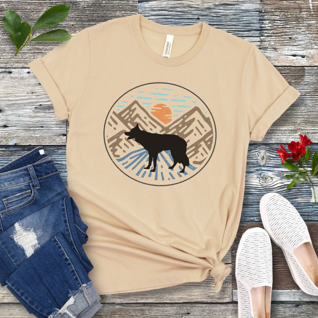 Cream colored t-shirt with a Border Collie dog in a vintage style mountain scene at sunset, shown on a wooden surface with jeans and shoes.