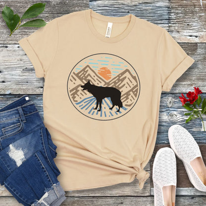 Cream colored t-shirt with a Border Collie dog in a vintage style mountain scene at sunset, shown on a wooden surface with jeans and shoes.