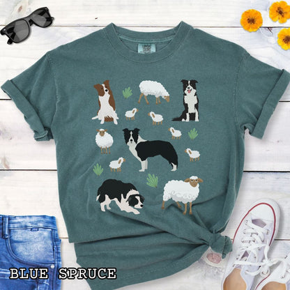 Green Comfort Colors  t-shirt with Border Collie dogs and grazing sheep, done in Cottage Core style, shown on a wooden surface with sunglasses and flowers.
