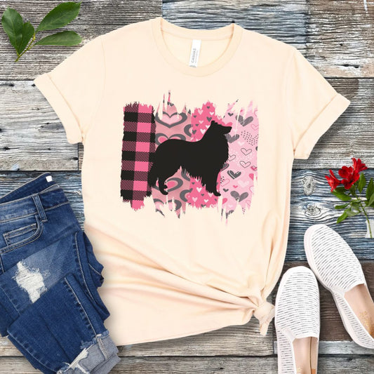 Beige Collie lover t-shirt with a black silhouette of a  Rough Collie on a pink and plaid brushstroke background, placed on a wooden surface with jeans and shoes.