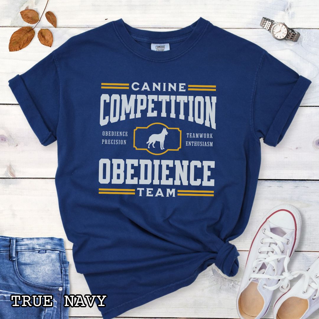 Navy Comfort Colors dog obedience t-shirt with 'Canine Competition Obedience Team' text and custom breed silhouette, presented on a wooden surface with denim jeans and a flower.