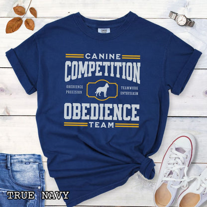 Navy Comfort Colors dog obedience t-shirt with 'Canine Competition Obedience Team' text and custom breed silhouette, presented on a wooden surface with denim jeans and a flower.