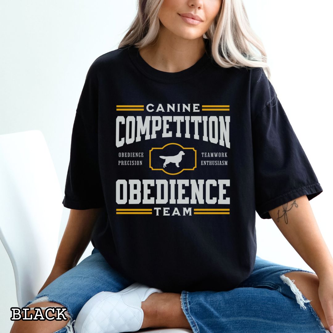 Black Comfort Colors dog obedience t-shirt with 'Canine Competition Obedience Team' text and custom breed silhouette, presented on a wooden surface with denim jeans and a flower.