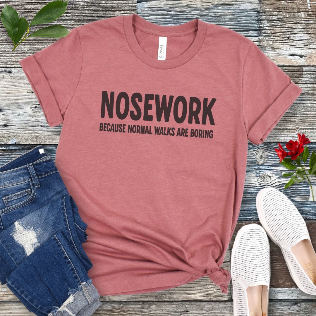 Mauve K9 Nose Work t-shirt with 'NOSEWORK BECAUSE NORMAL WALKS ARE BORING' text on a wooden surface with jeans and shoes.