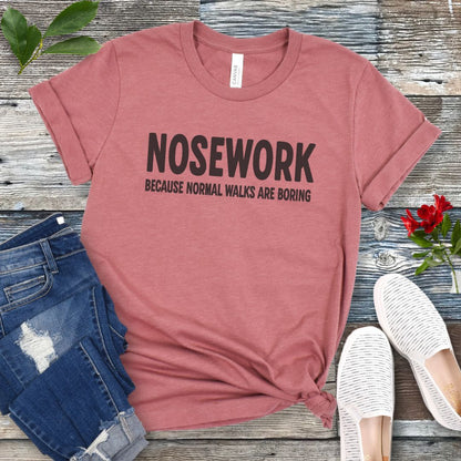 Mauve K9 Nose Work t-shirt with 'NOSEWORK BECAUSE NORMAL WALKS ARE BORING' text on a wooden surface with jeans and shoes.