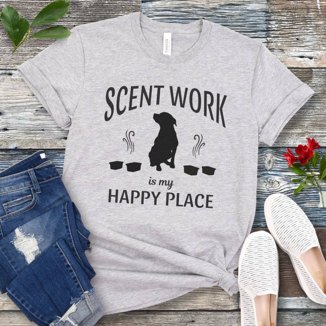 Grey t-shirt with 'Scent Work is my Happy Place' text and dog silhouette on a wooden surface with jeans and shoes.